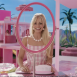 Margot Robbie as Barbie sits at a pink vanity, smiling into a big round mirror.